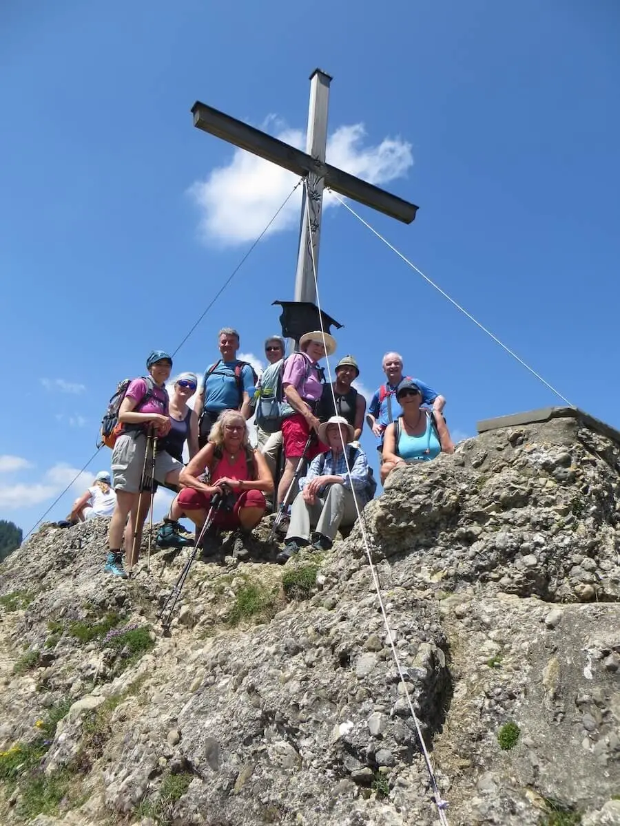 Wandergruppe am Gipfelkreuz des Bärenköpfle bei Sonnenschein, umgeben von Felsen und blauem Himmel, nach erfolgreichem Aufstieg. | © DAV Markt Schwaben