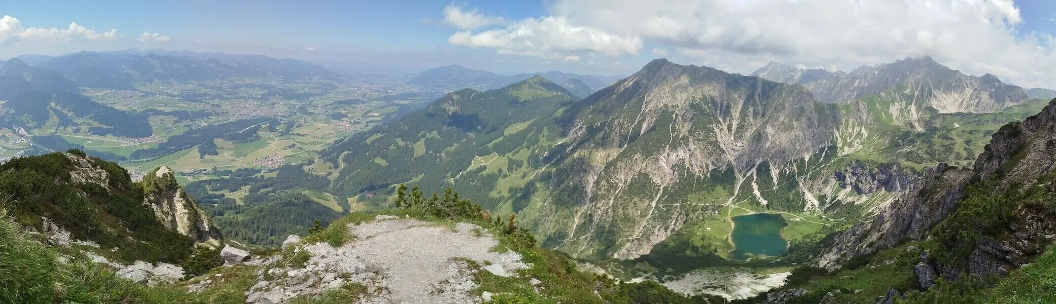 Blick vom Rubihorn über grüne Täler, alpine Seen und felsige Gipfel unter teils bewölktem Himmel – ein Moment voller Weite. | © DAV Markt Schwaben