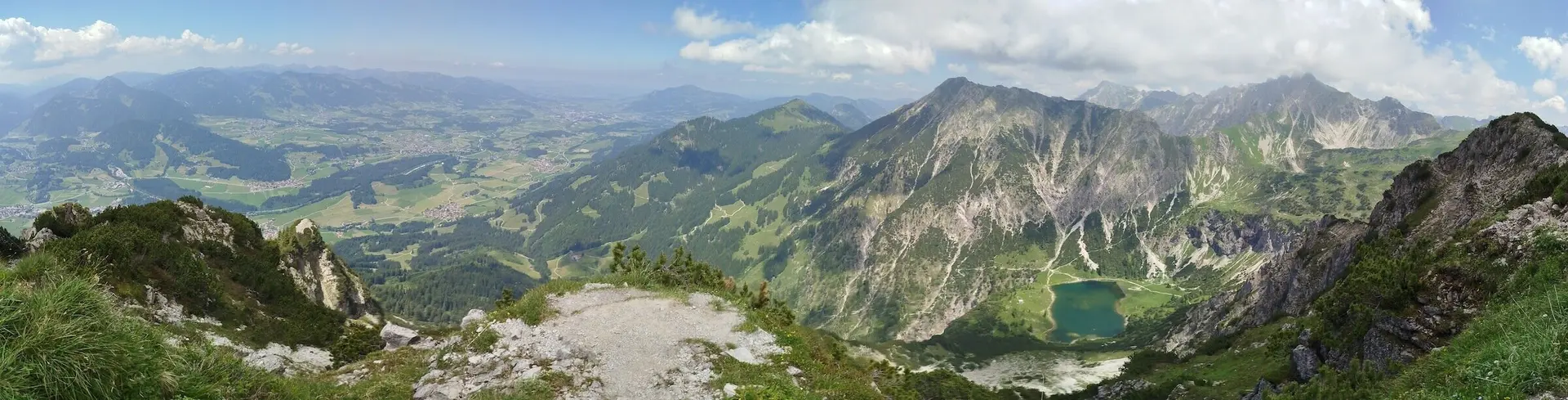 Blick vom Rubihorn über grüne Täler, alpine Seen und felsige Gipfel unter teils bewölktem Himmel – ein Moment voller Weite. | © DAV Markt Schwaben