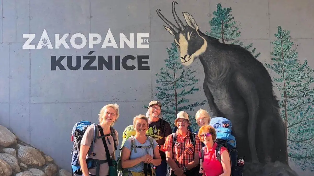 Sechs Wandernde mit Rucksäcken stehen vor einem Wandbild mit Tatra-Gämse und Schriftzug „Zakopane Kuźnice“ auf Betonwand. | © DAV Markt Schwaben | Foto Hildegard Petschik
