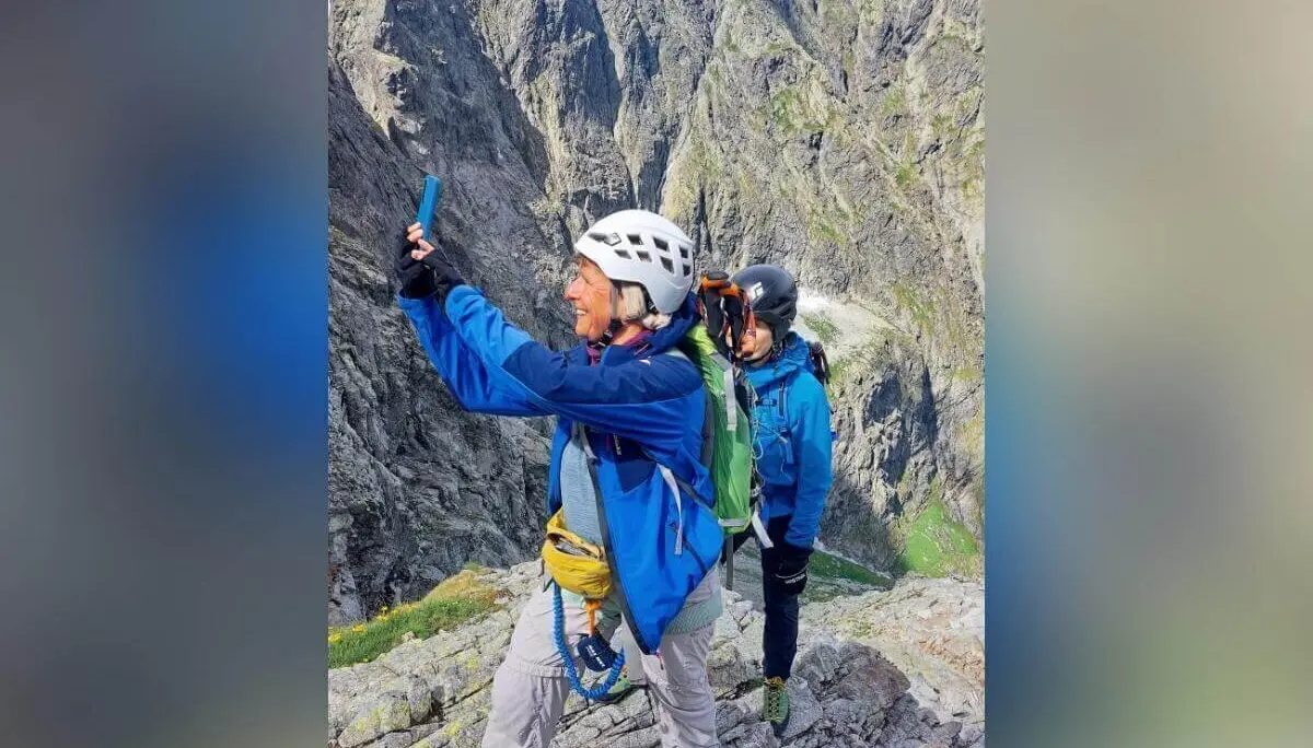 Zwei Kletternde mit Helm und Gurt stehen auf felsigem Berggrat; eine Person fotografiert, dahinter steile Gipfel und Wolken. | © DAV Markt Schwaben | Foto Lutz Gründel
