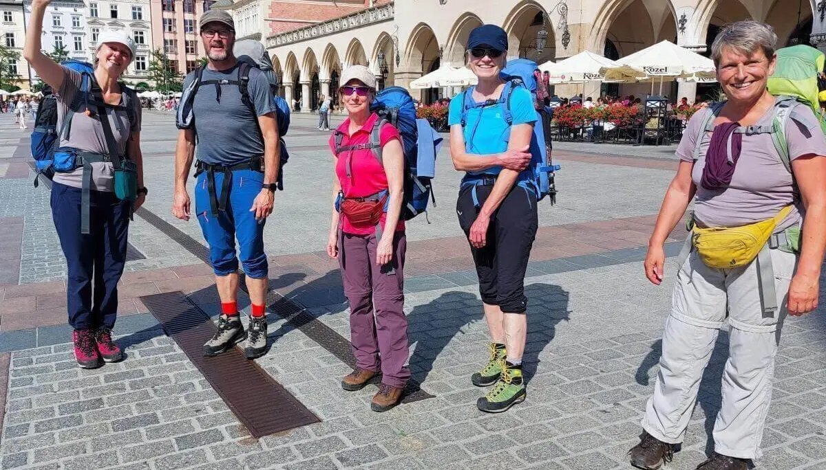 Fünf Wandernde mit großen Rucksäcken stehen auf Kopfsteinpflaster vor historischen Gebäuden mit Arkaden und Café-Terrassen. | © DAV Markt Schwaben | Foto Lutz Gründel