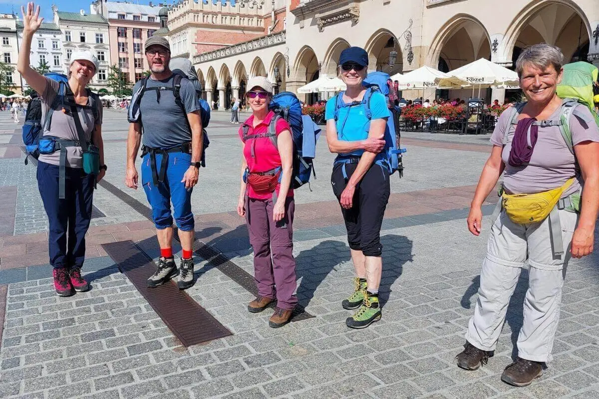 Fünf Wandernde mit großen Rucksäcken stehen auf Kopfsteinpflaster vor historischen Gebäuden mit Arkaden und Café-Terrassen. | © DAV Markt Schwaben | Foto Lutz Gründel