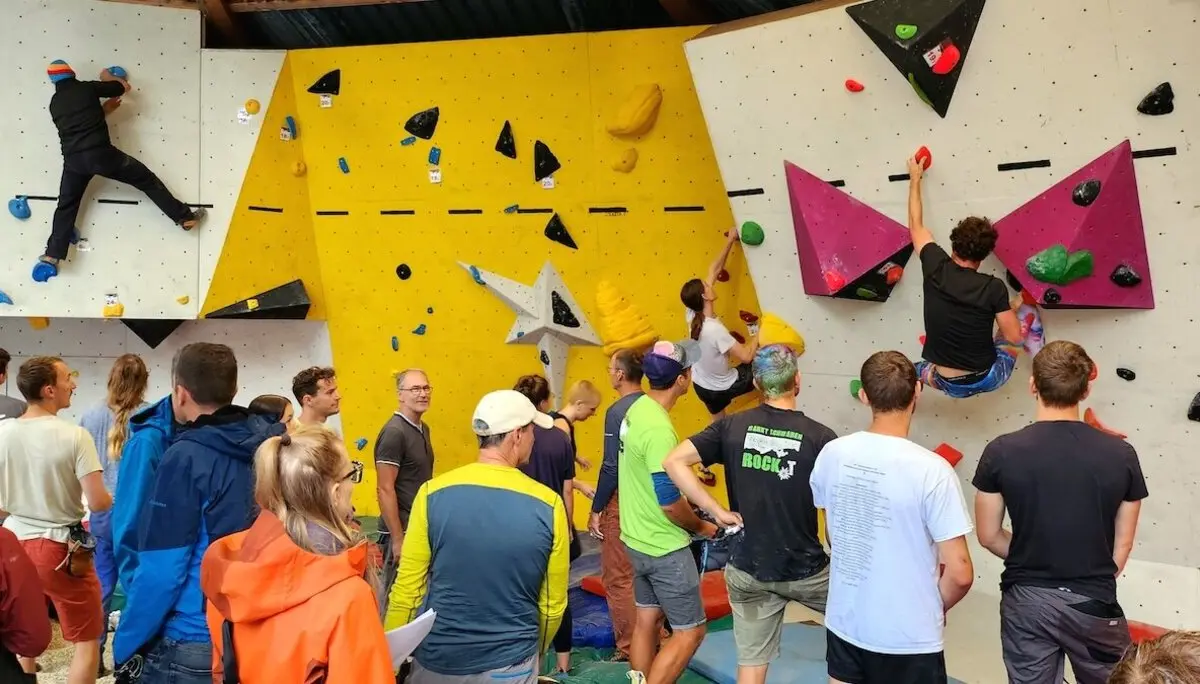 Mehrere Kletternde erklimmen die Boulderwand, während Zuschauer gespannt das Geschehen im Kletterzentrum verfolgen. | © DAV Markt Schwaben | Foto Anna Thoms