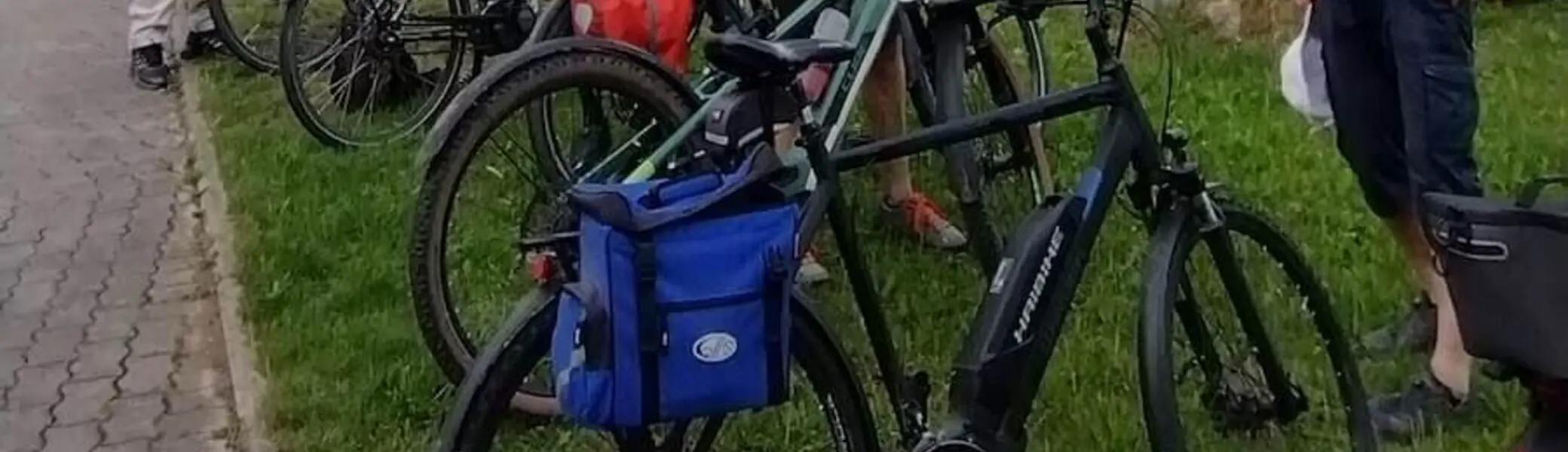 Fünf ältere Radfahrer stehen mit Gepäcktaschen vor einem Ortsschild – Helm, Kirche und Tourenausrüstung im Blick. | © DAV Markt Schwaben