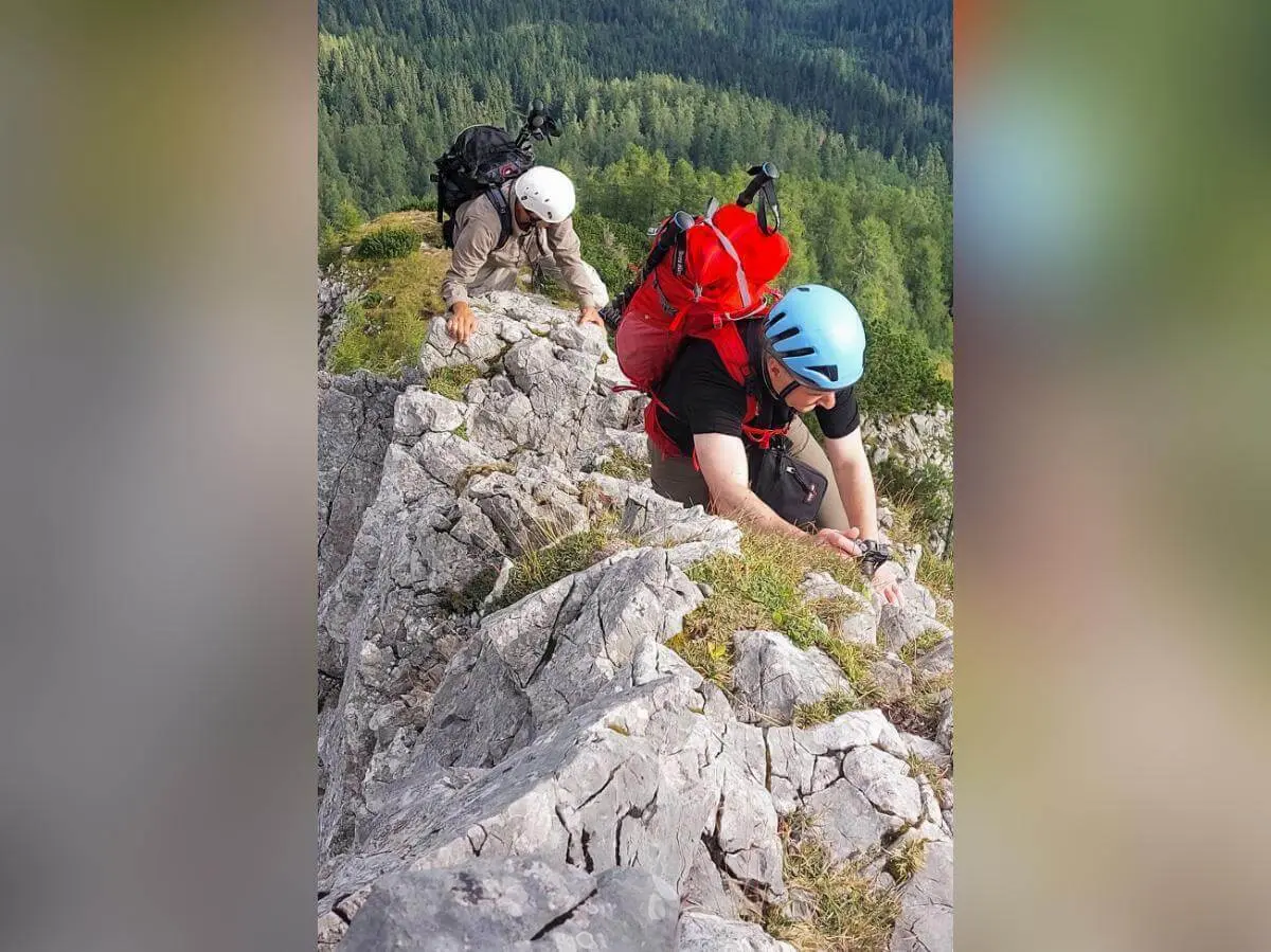 Zwei Bergsteiger sichern sich auf steiler Felskante, im Hintergrund Waldhang und felsige Bergflanke. | © DAV Markt Schwaben · Foto: Lutz Gründel