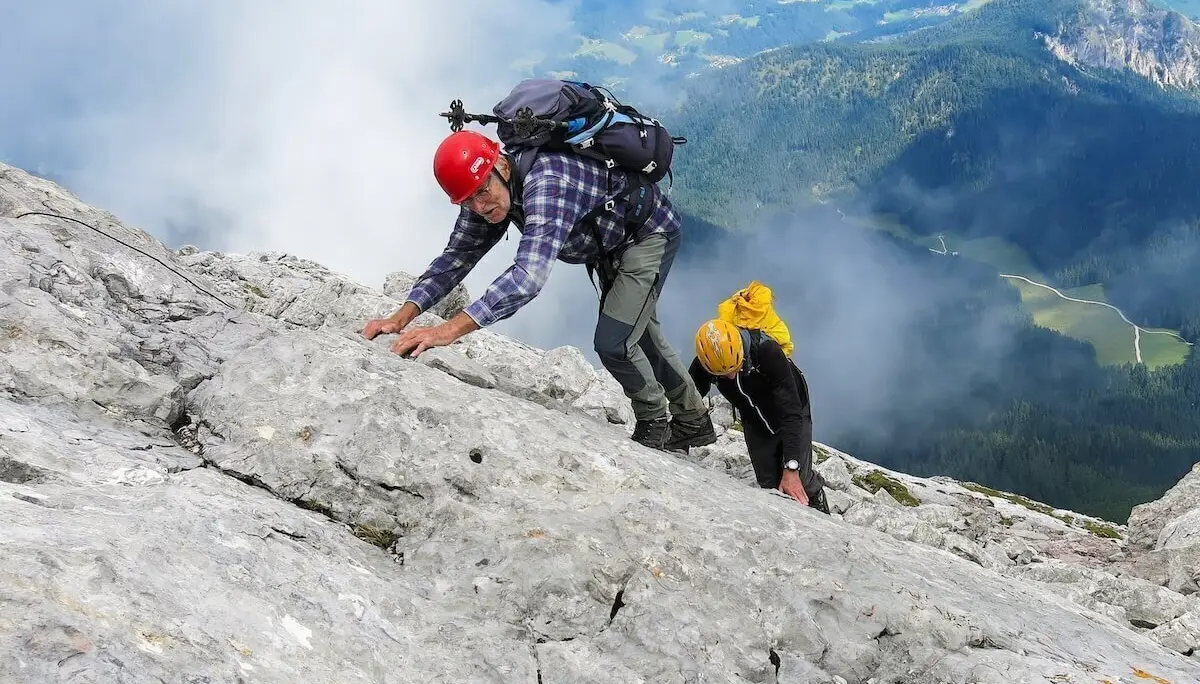 Zwei Bergsteiger sichern sich am steilen Fels, hinten bewaldete Täler und Wolken über Bergflanken. | © DAV Markt Schwaben · Foto: Erwin Matzinger