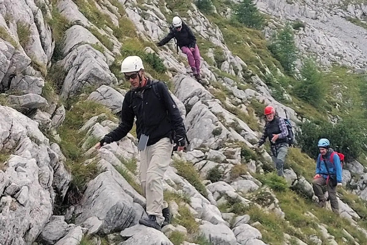 Vier Bergsteiger steigen über felsiges Gelände mit Grasinseln ab, im Hintergrund steiler Bergwald. | © DAV Markt Schwaben · Foto: Lutz Gründel