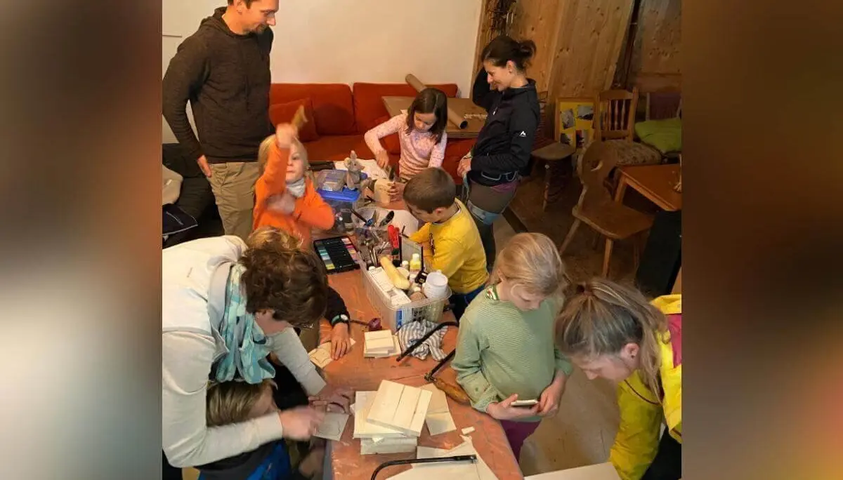 Kinder und Erwachsene gestalten am Basteltisch farbenfrohe Holzobjekte; im Hintergrund ein Holzspielhaus. | © DAV Markt Schwaben | Foto: Helena De Monte