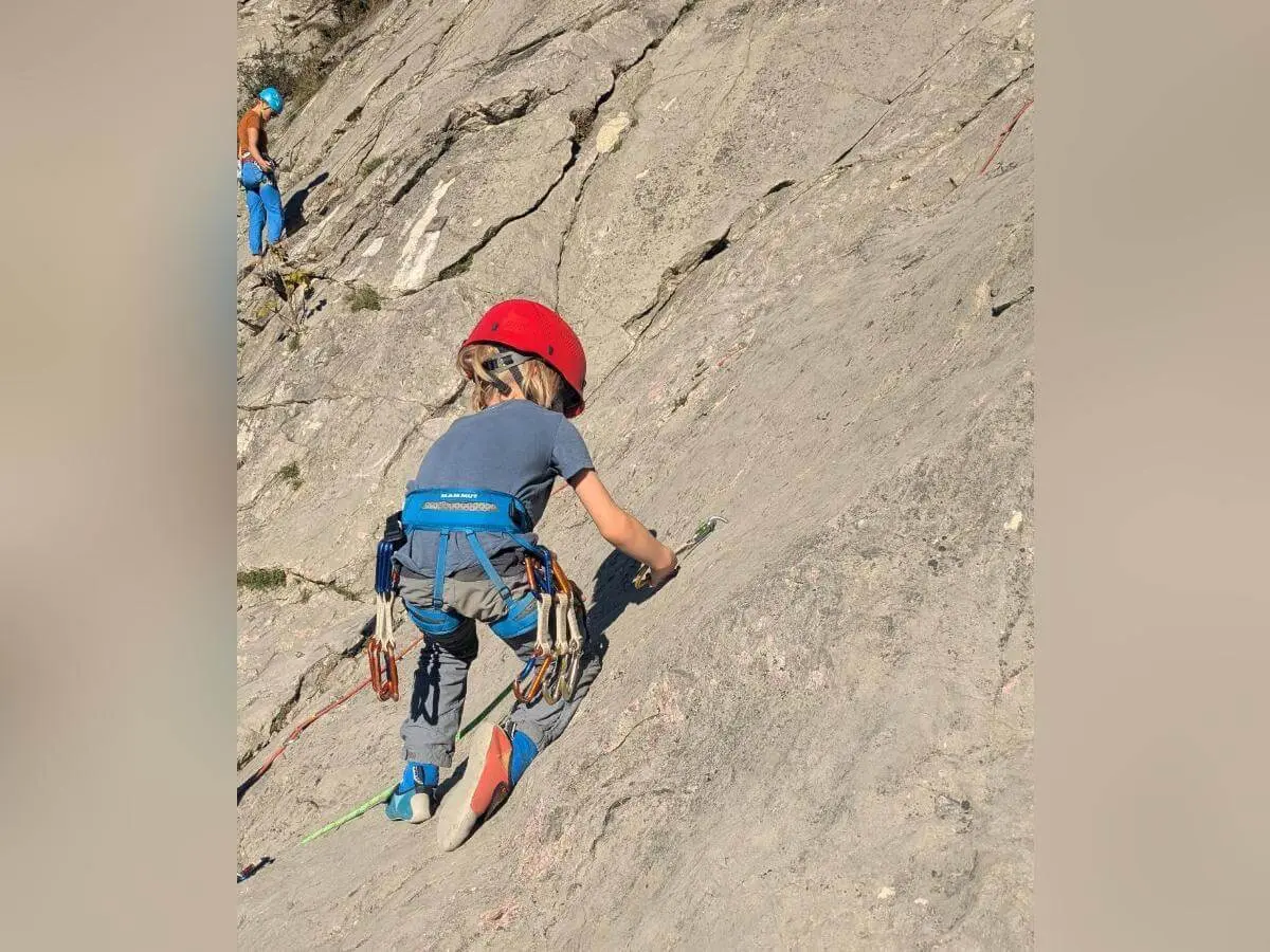 Zwei Kinder mit Helmen stehen auf einer Wiese vor einem Felsen und hantieren gemeinsam mit einem Kletterseil. Im Hintergrund sind ein Weinberg, Herbstlaub und eine felsige Landschaft zu sehen. | © DAV Markt Schwaben · Foto: Silke Titze