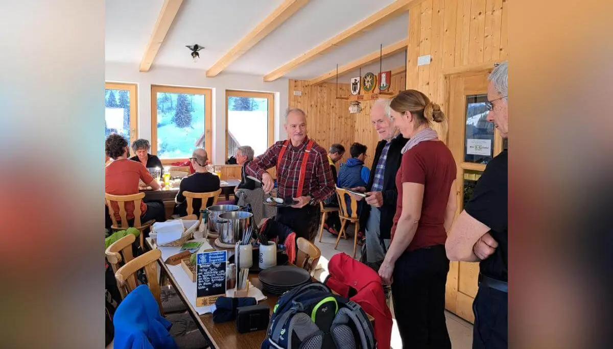 Wandergruppe beim Abendessen in holzgetäfeltem Gastraum, Fensterblick auf verschneite Landschaft, Menütafel im Vordergrund. | © DAV Markt Schwaben · Foto Tanja Döhler