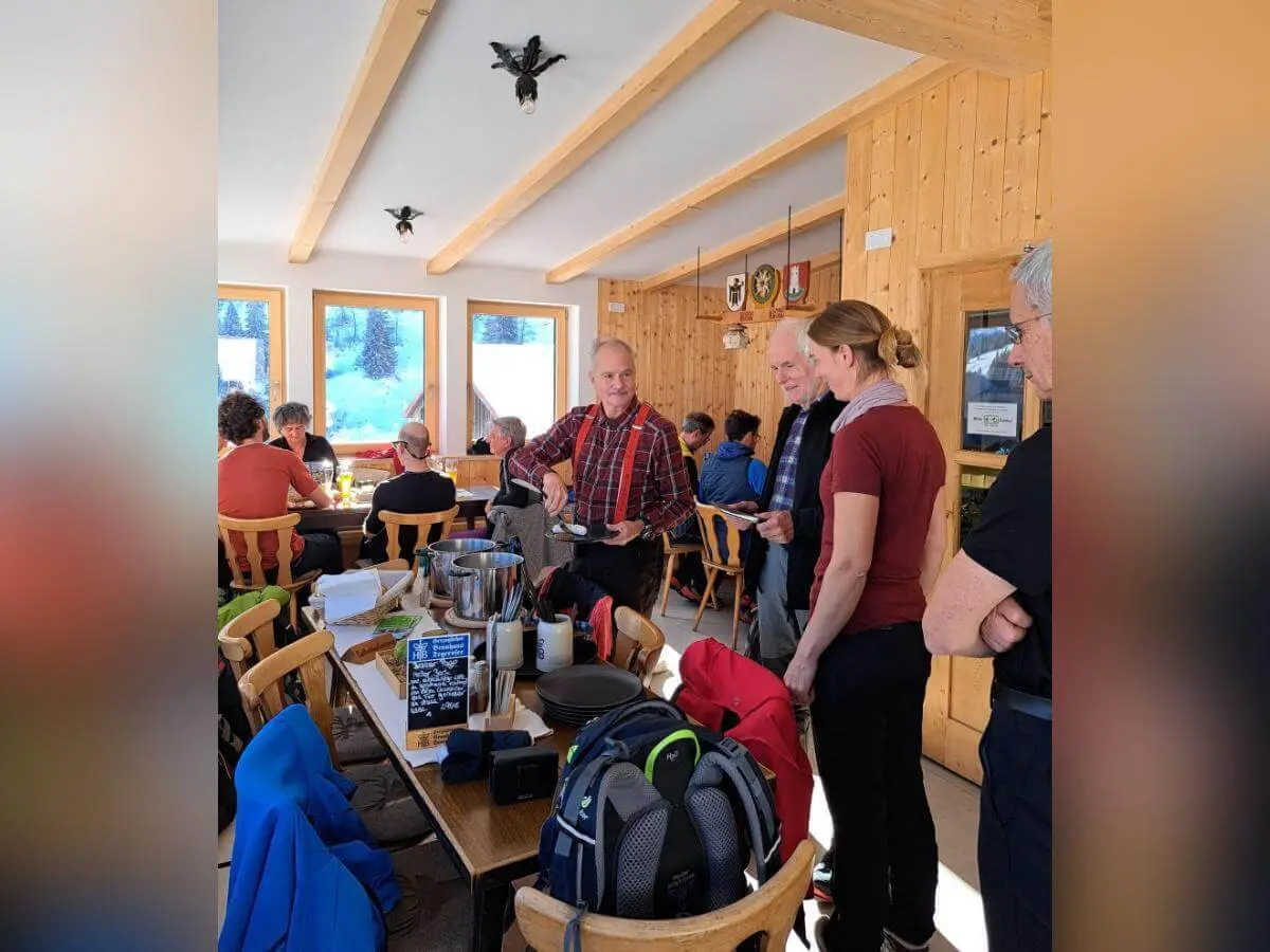 Wandergruppe beim Abendessen in holzgetäfeltem Gastraum, Fensterblick auf verschneite Landschaft, Menütafel im Vordergrund. | © DAV Markt Schwaben · Foto Tanja Döhler