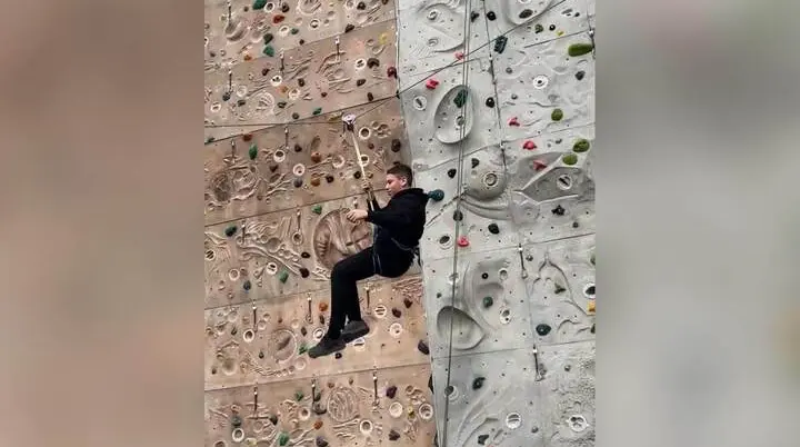 Ein Jugendlicher der Jugendgruppe hängt gesichert an einem Seil vor einer Indoor‑Kletterwand und führt eine Schaukelbewegung aus. | © DAV Mark Schwaben / Wiebke Rauschenbach 