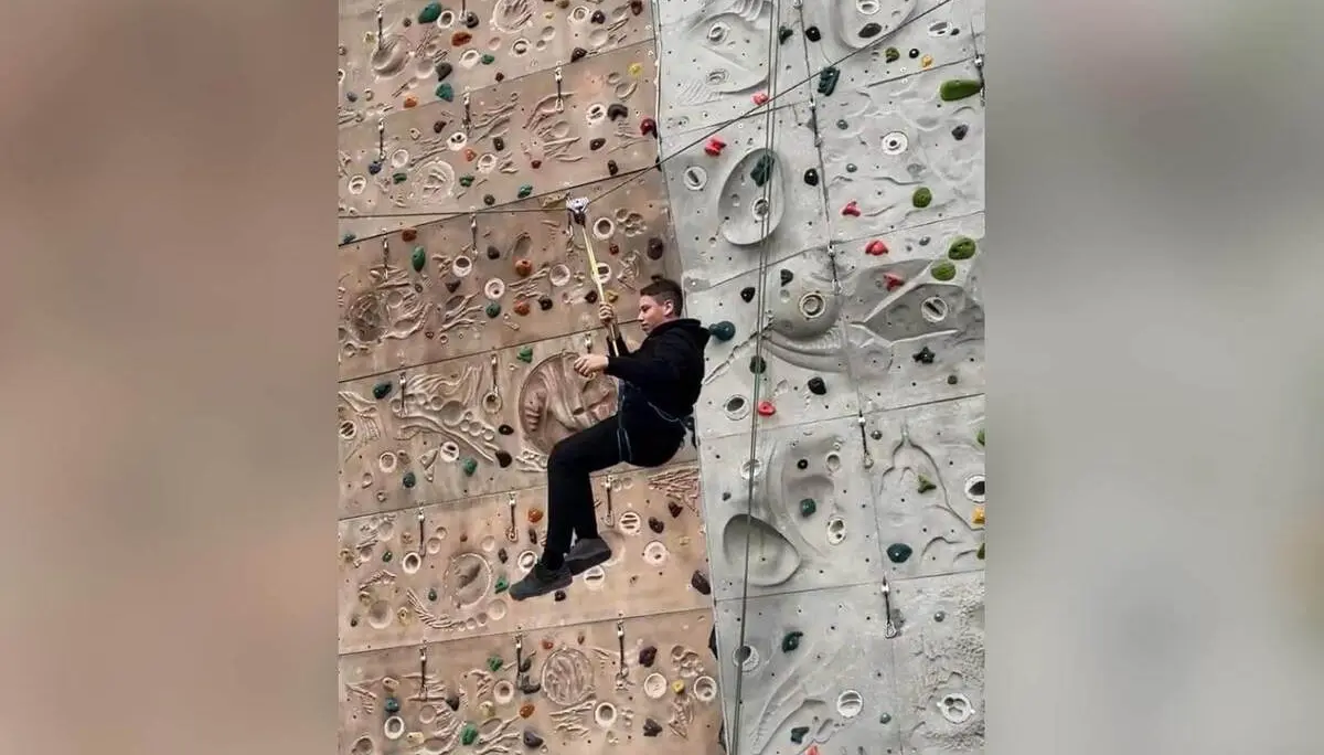 Ein Jugendlicher der Jugendgruppe hängt gesichert an einem Seil vor einer Indoor‑Kletterwand und führt eine Schaukelbewegung aus. | © DAV Mark Schwaben / Wiebke Rauschenbach 