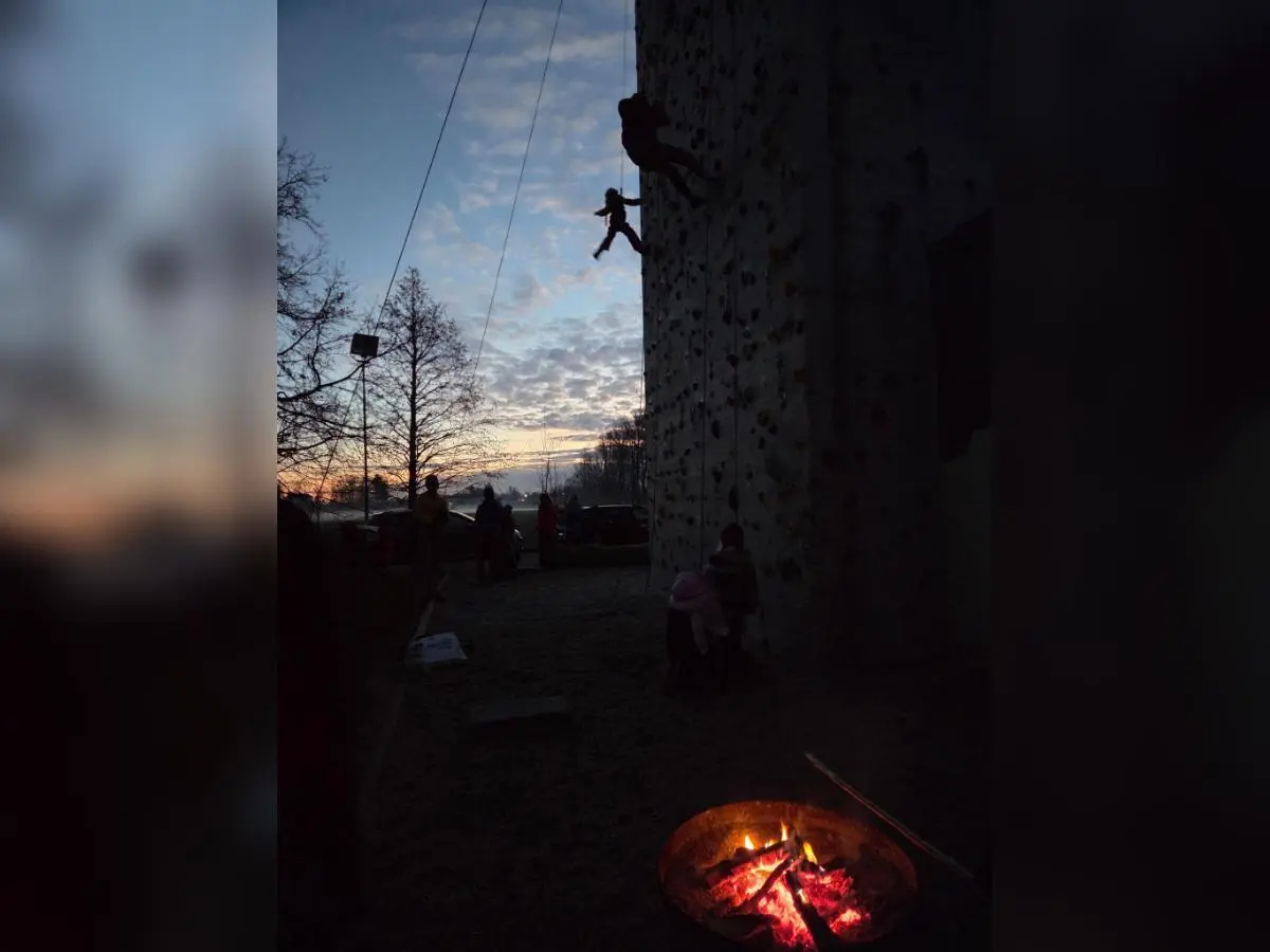 Kinder und Erwachsene beim Klettern an der beleuchteten Wand; im Vordergrund Feuerschale, dahinter Abendhimmel und Bäume. | © DAV Markt Schwaben · Familiengruppe