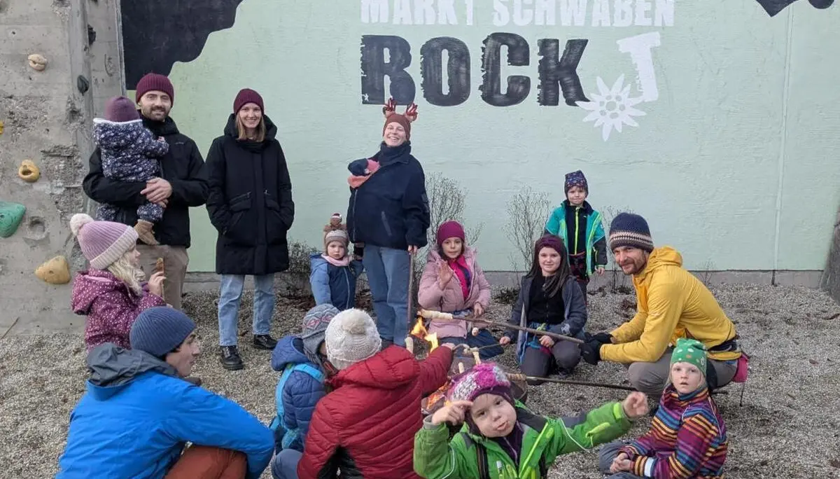Kinder und Erwachsene stehen vor bemalter Kletterwand mit Feuerstelle; Winterkleidung, lockere Gruppe, Dämmerung. | © DAV Markt Schwaben · Familiengruppe