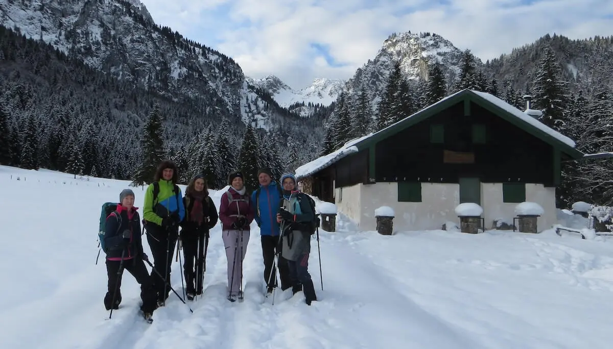 Sechs Wandernde stehen auf einem verschneiten Weg vor der Kirchsteinhütte; im Hintergrund Tannenwald und Berggipfel im Schnee. | © DAV Markt Schwaben | Foto: Gerlinde Hübl