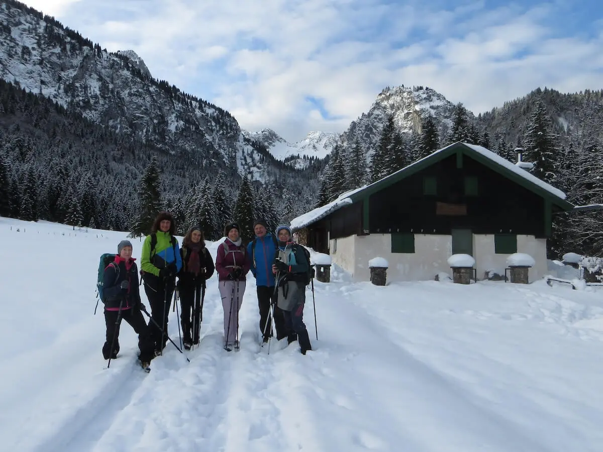 Sechs Wandernde stehen auf einem verschneiten Weg vor der Kirchsteinhütte; im Hintergrund Tannenwald und Berggipfel im Schnee. | © DAV Markt Schwaben | Foto: Gerlinde Hübl