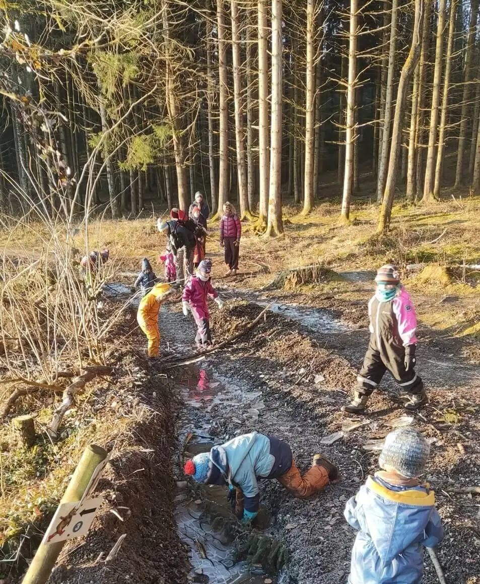 Kinder und Erwachsene spielen auf einem matschigen Waldweg mit Pfützen, umgeben von kahlen Bäumen. | © DAV Markt Schwaben Familiengruppe