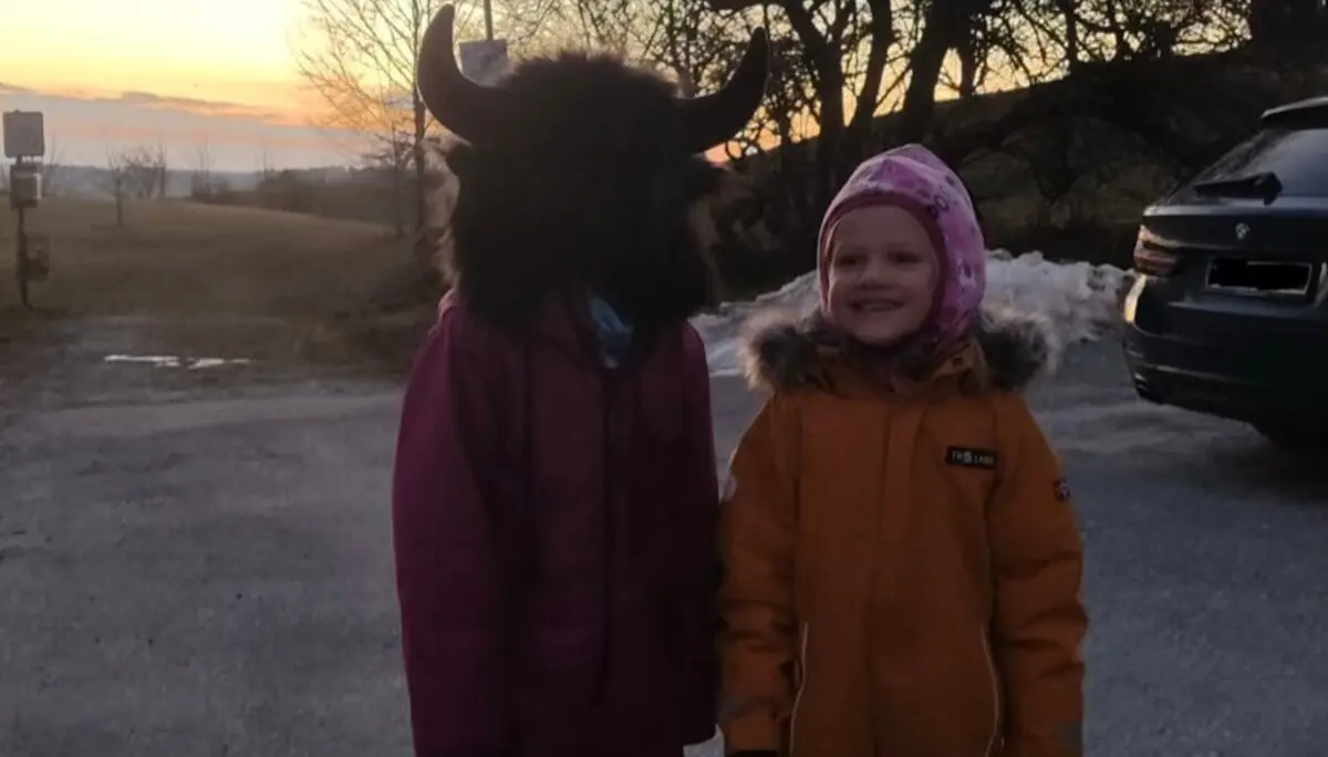 Zwei Kinder im Schneeanzug stehen bei Sonnenuntergang draußen, eines trägt eine Fellmütze mit Hörnern. | © DAV Markt Schwaben Familiengruppe