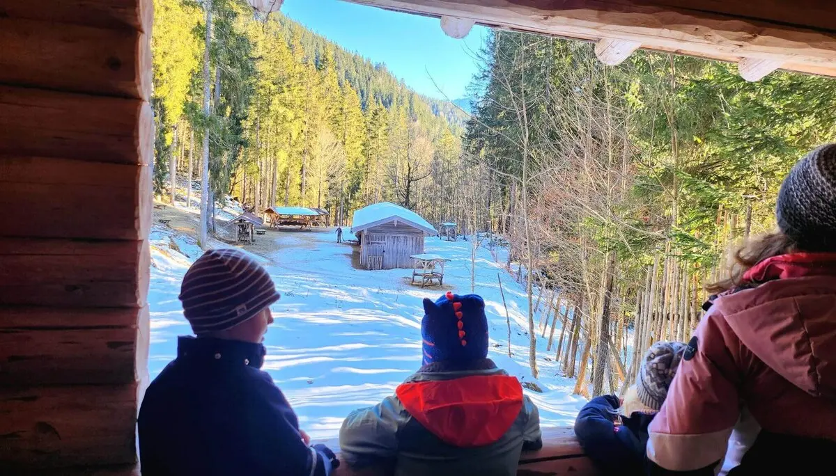 Drei Kinder und ein Erwachsener beobachten aufgeregt die Hirschfütterung aus der Ferne in einer verschneiten Waldlandschaft. | © DAV Markt Schwaben