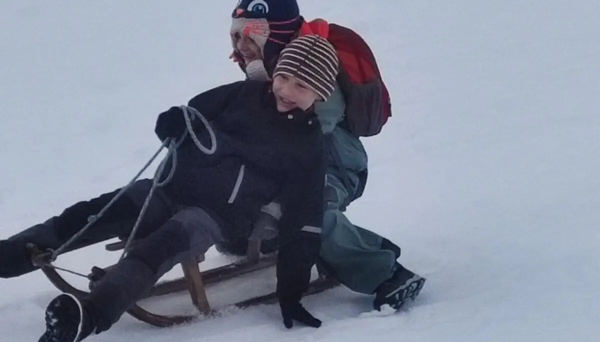 Zwei Kinder auf einem Schlitten fahren lachend einen Hügel hinunter. | © DAV Markt Schwaben
