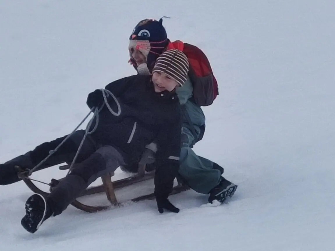 Zwei Kinder auf einem Schlitten fahren lachend einen Hügel hinunter. | © DAV Markt Schwaben