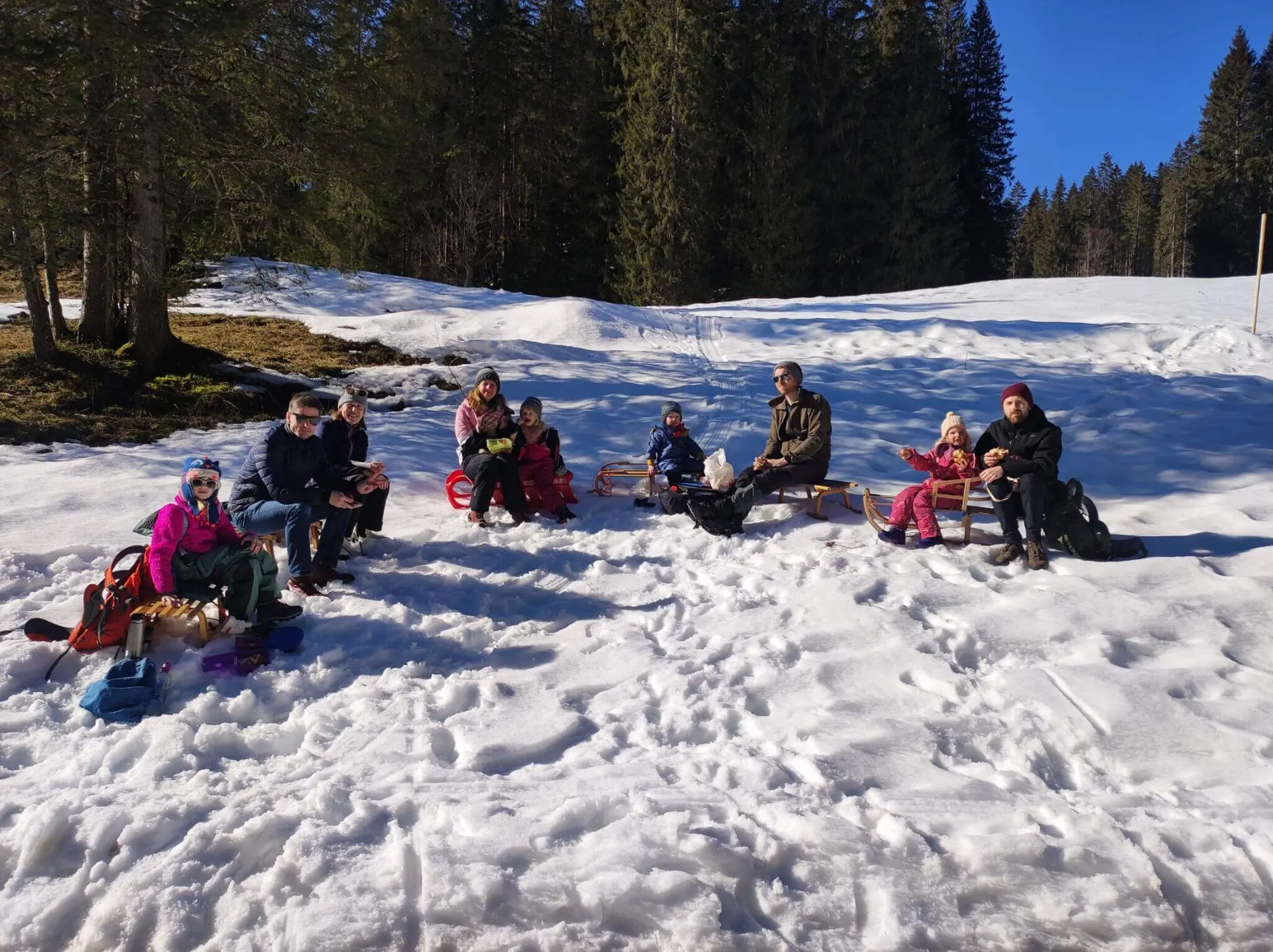Gruppe von Menschen sitzt im Schnee auf Schlitten und genießt eine Brotzeit, umgeben von hohen Bäumen und winterlicher Stimmung. | © DAV Markt Schwaben