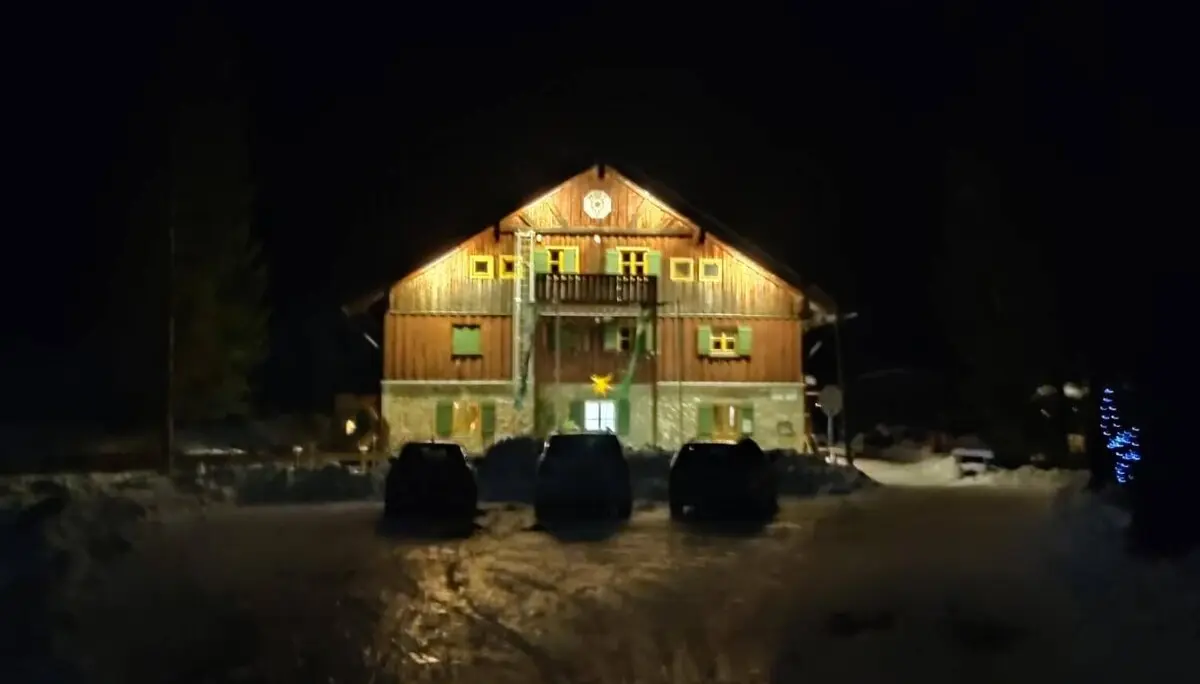 Zweistöckige Hütte mit beleuchteter braun-grüner Fassade, verschneitem Dach in der tiefen Nacht." | © DAV Markt Schwaben