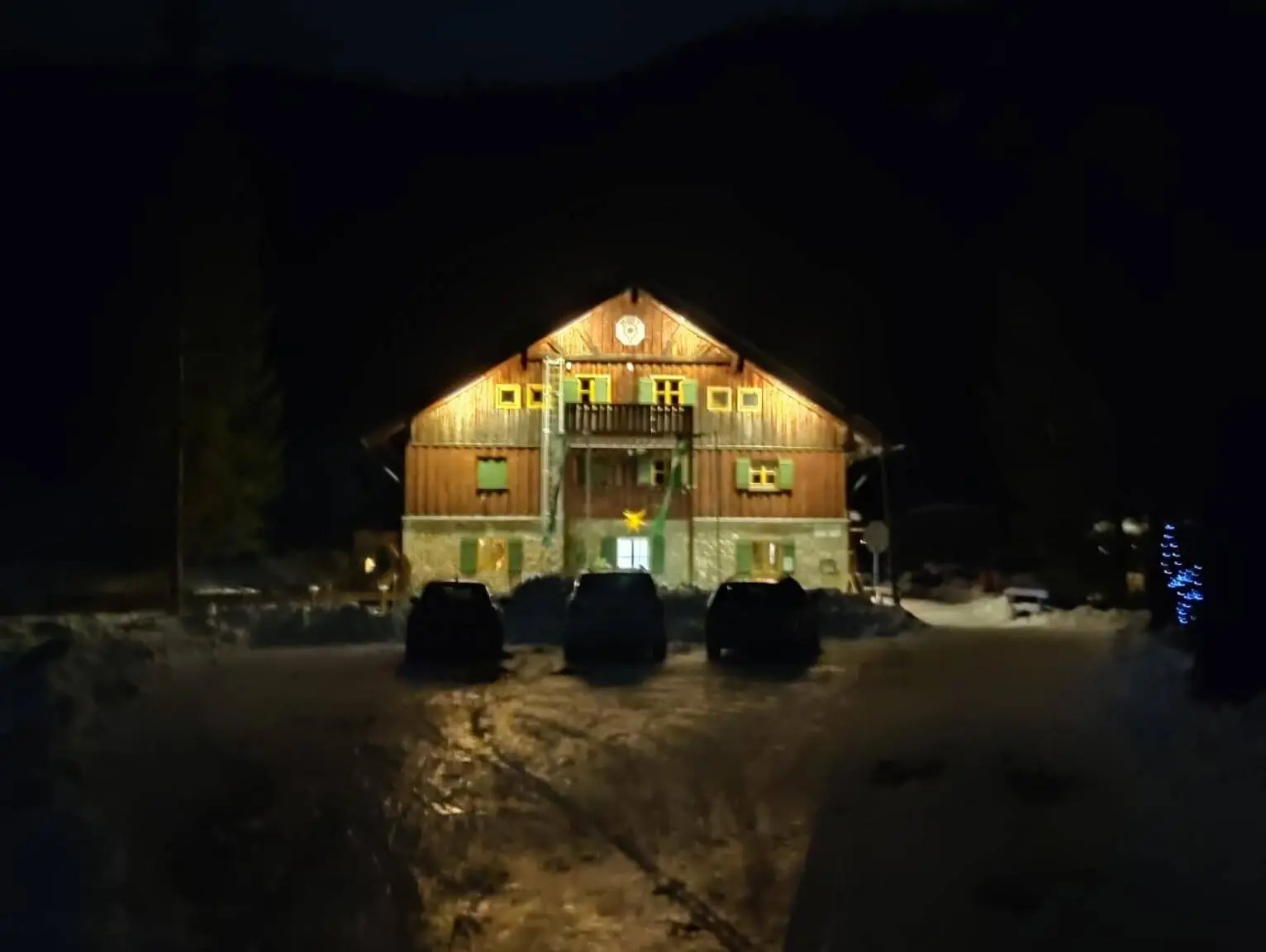 Zweistöckige Hütte mit beleuchteter braun-grüner Fassade, verschneitem Dach in der tiefen Nacht." | © DAV Markt Schwaben