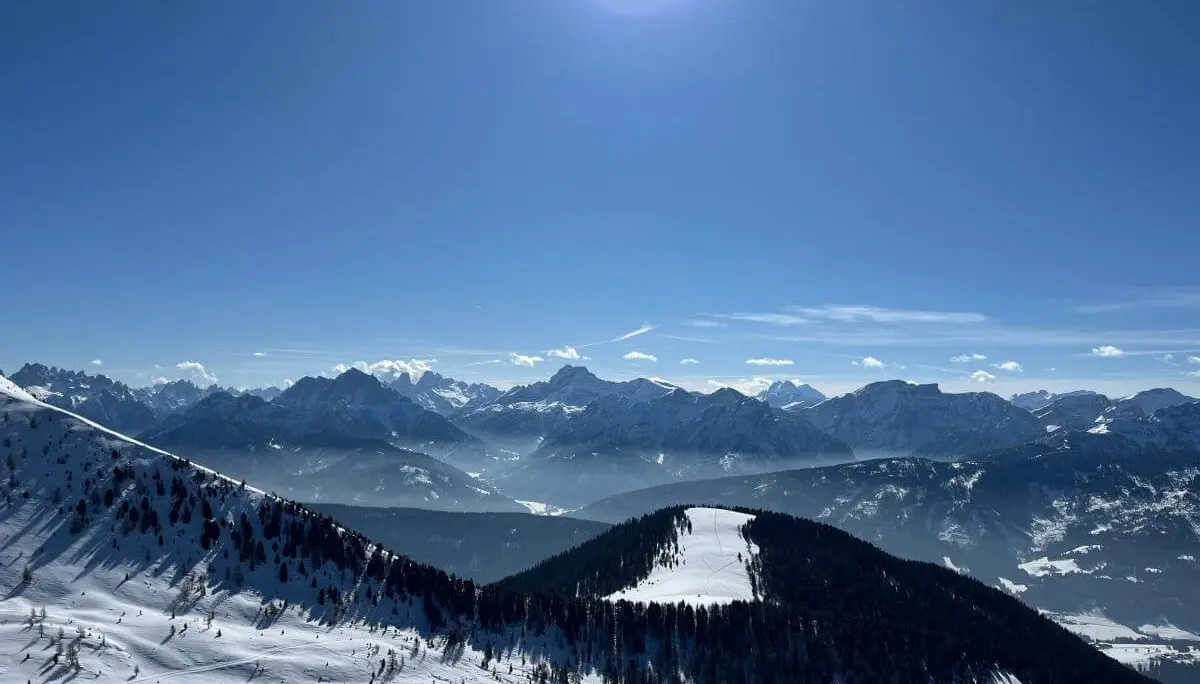 Sonnenbeschienener Dolomitenhang mit Skispuren und Blick auf bewaldeten Grat; im Hintergrund schroffe Gipfel und blauer Himmel. | © DAV Markt Schwaben · Foto: Peter Langenbacher