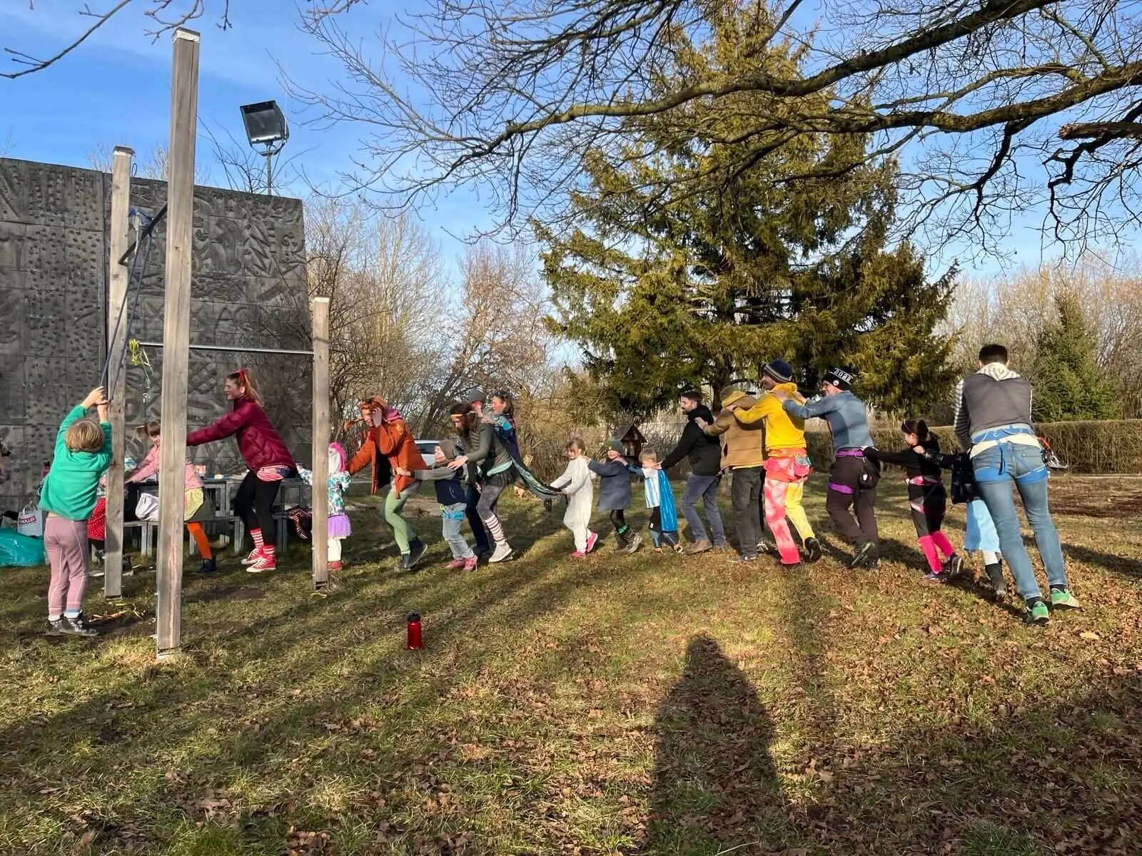 Eine Gruppe von Erwachsenen und Kindern in farbenfrohen und verspielten Outfits draußen auf einer Wiese, lächelnd und mit Spaß bei einer Polonaise. | © DAV Markt Schwaben