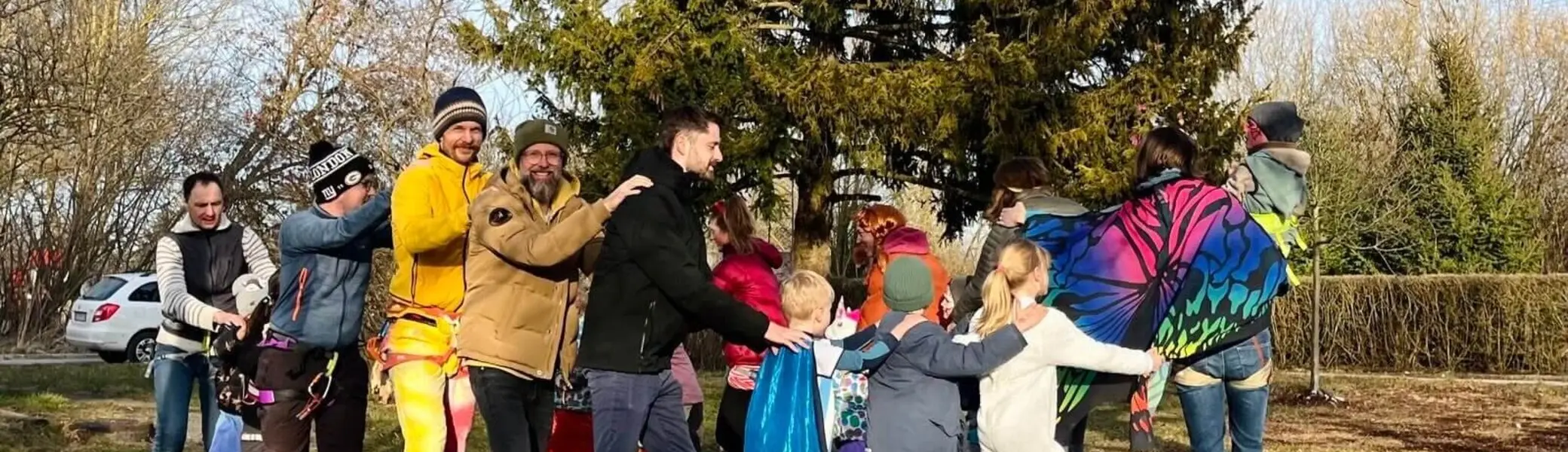 Eine Gruppe von Erwachsenen und Kindern in farbenfrohen und verspielten Outfits draußen auf einer Wiese, lächelnd und mit Spaß bei einer Polonaise. | © DAV Markt Schwaben