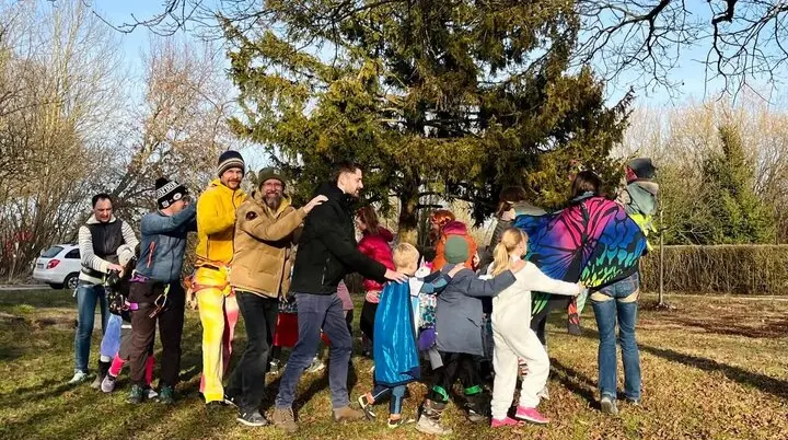 Eine Gruppe von Erwachsenen und Kindern in farbenfrohen und verspielten Outfits draußen auf einer Wiese, lächelnd und mit Spaß bei einer Polonaise. | © DAV Markt Schwaben