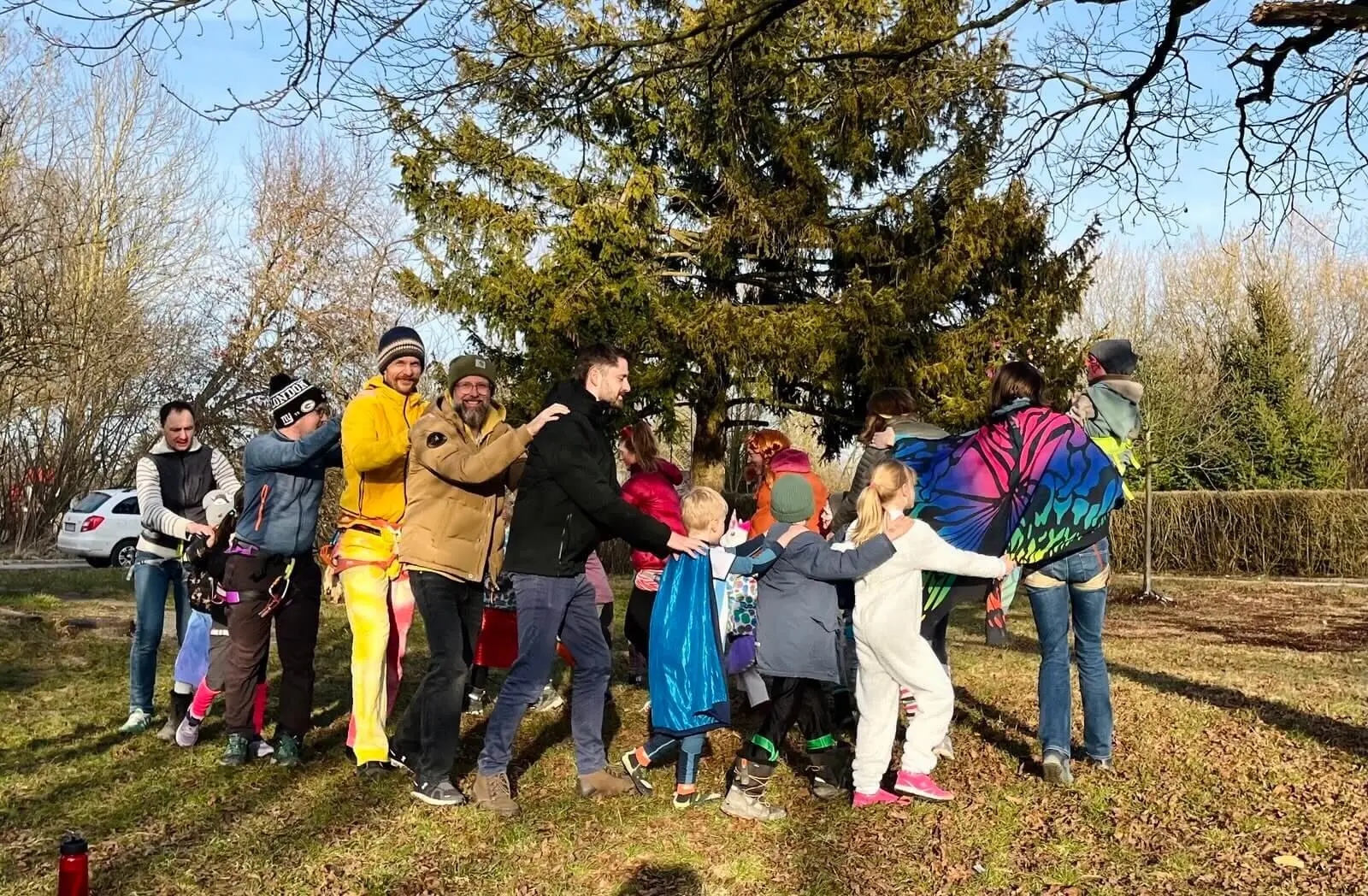 Eine Gruppe von Erwachsenen und Kindern in farbenfrohen und verspielten Outfits draußen auf einer Wiese, lächelnd und mit Spaß bei einer Polonaise. | © DAV Markt Schwaben