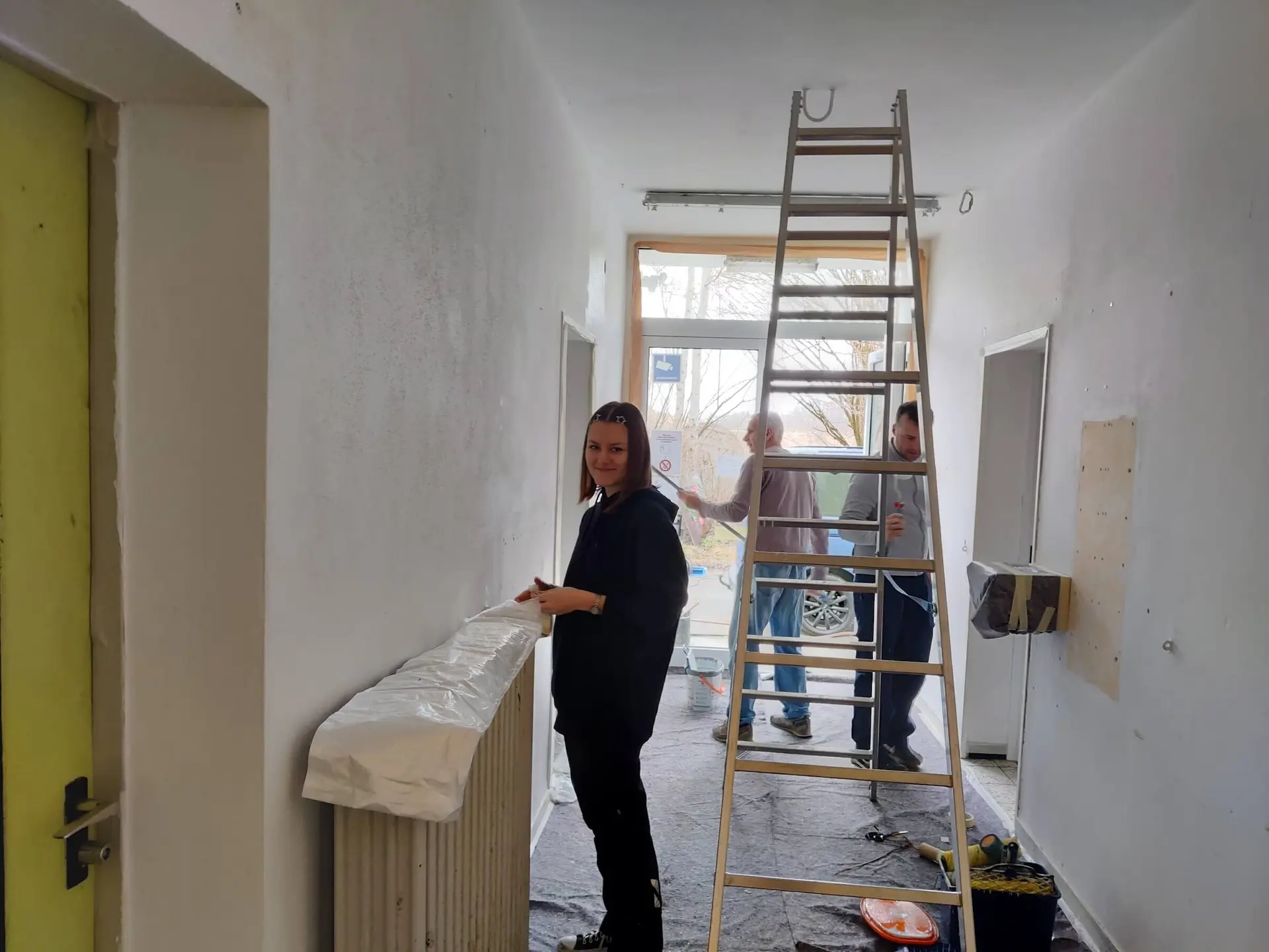 Ein Mitglied im Vordergrund, eine Leiter und zwei weitere Mitglieder, die den Flur während des Arbeitsdienstes im März 2025 streichen. | © DAV Markt Schwaben