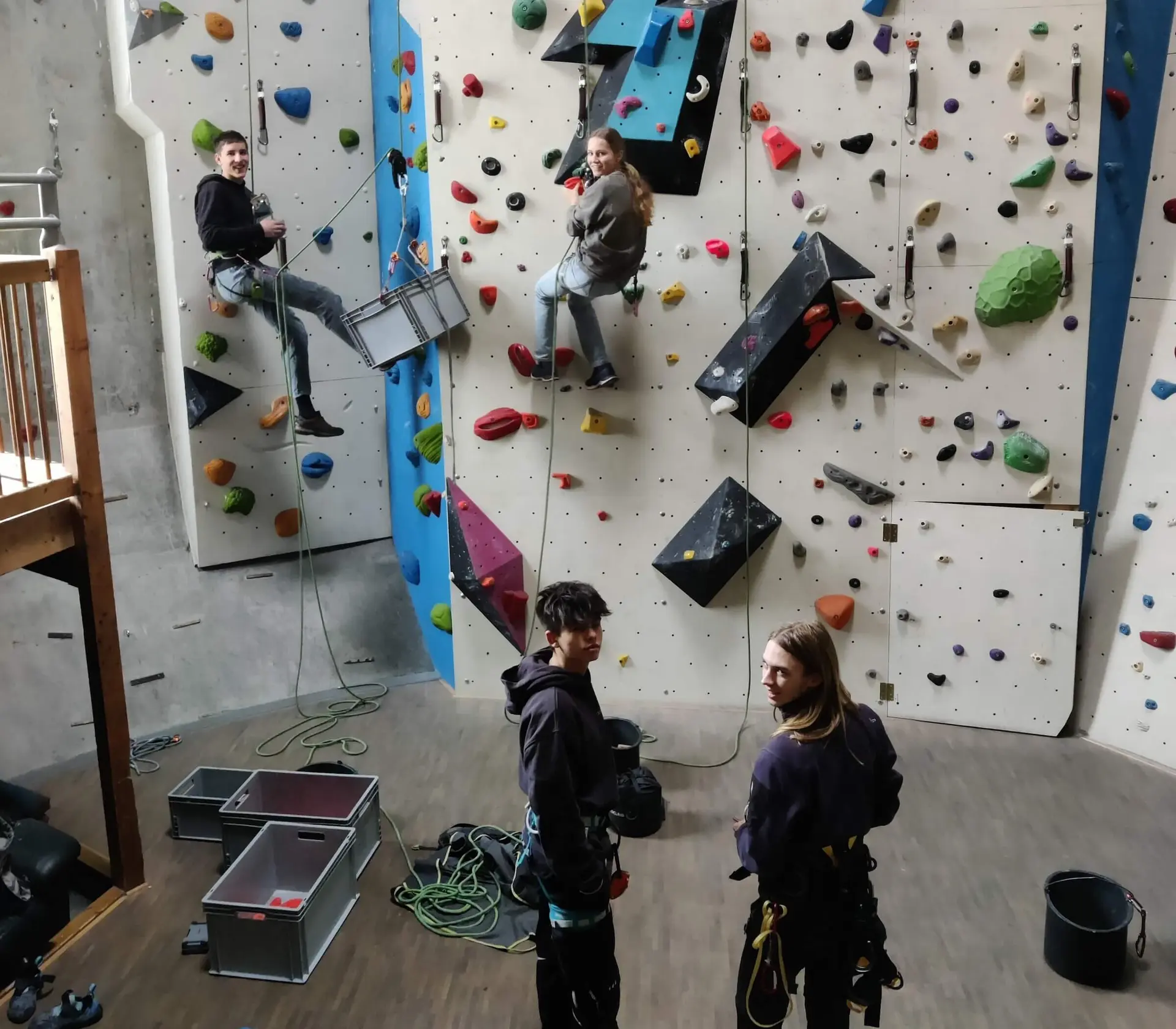 Vier Personen in einer Indoor-Kletterhalle, zwei klettern gesichert, zwei beobachten mit Kletterausrüstung | © DAV Markt Schwaben