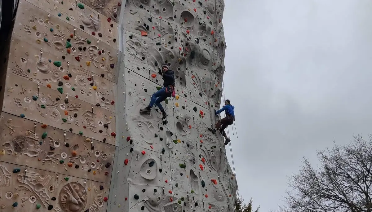 Zwei Personen klettern an einer großen Outdoor-Kletterwand mit bunten Griffen. | © DAV Markt Schwaben