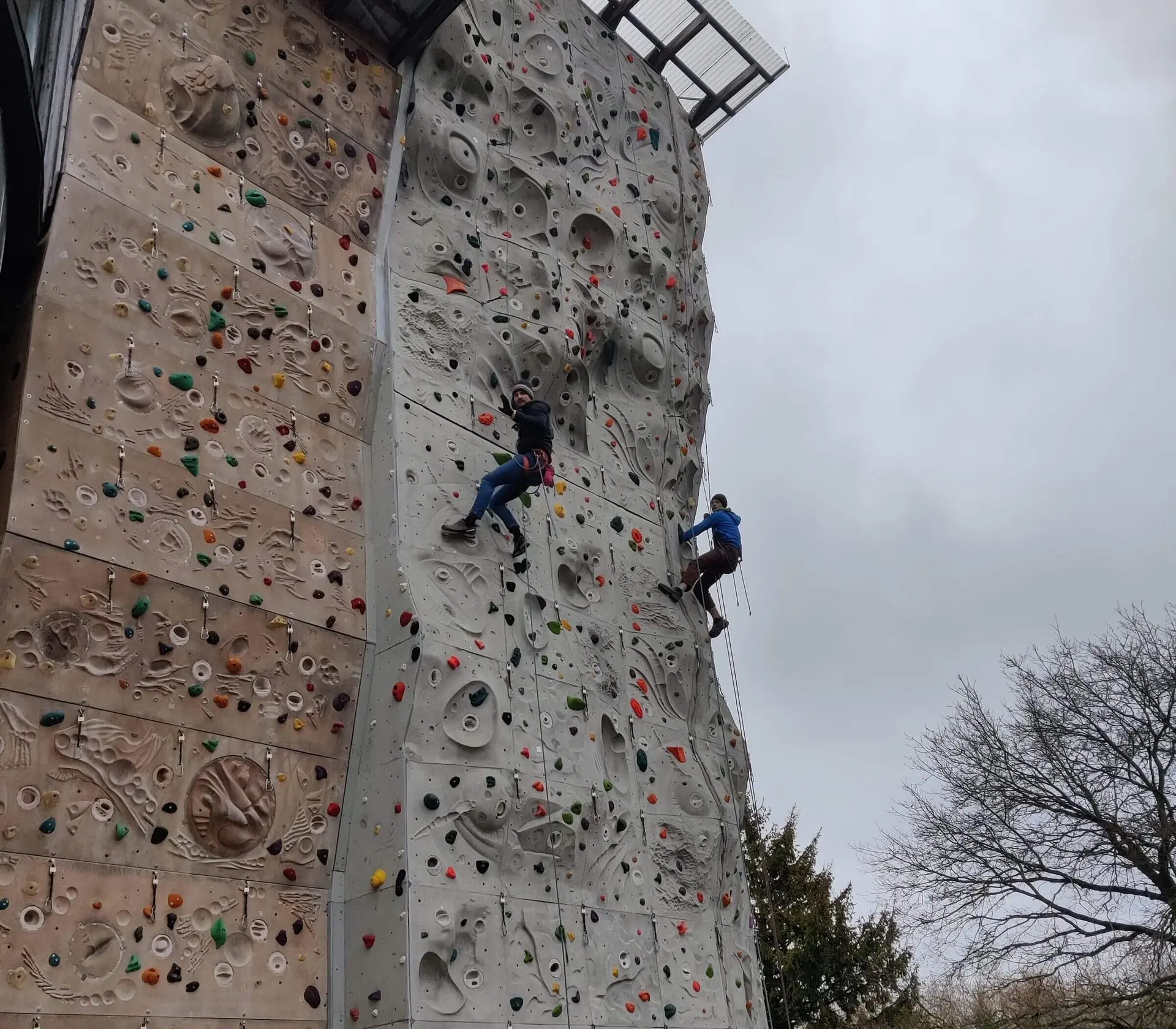 Zwei Personen klettern an einer großen Outdoor-Kletterwand mit bunten Griffen. | © DAV Markt Schwaben