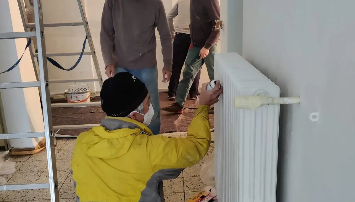 Ein Mitglied streicht einen Heizkörper, während andere Mitglieder im Hintergrund vorbeigehen während des Arbeitsdienstes. | © DAV Markt Schwaben