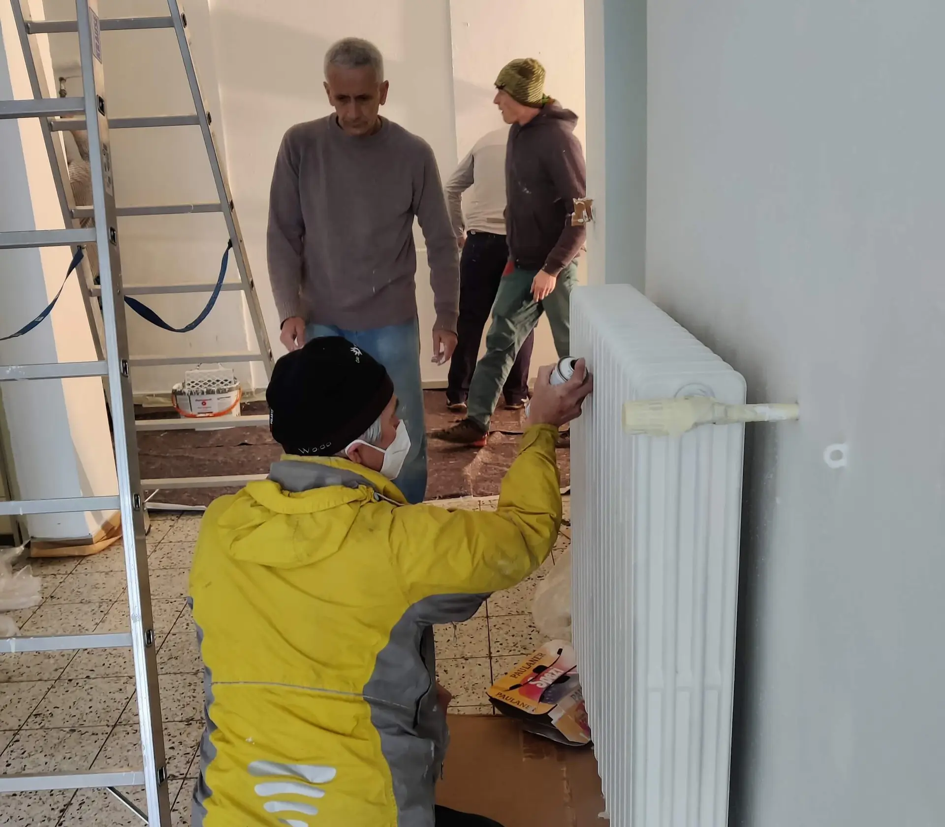 Ein Mitglied streicht einen Heizkörper, während andere Mitglieder im Hintergrund vorbeigehen während des Arbeitsdienstes. | © DAV Markt Schwaben