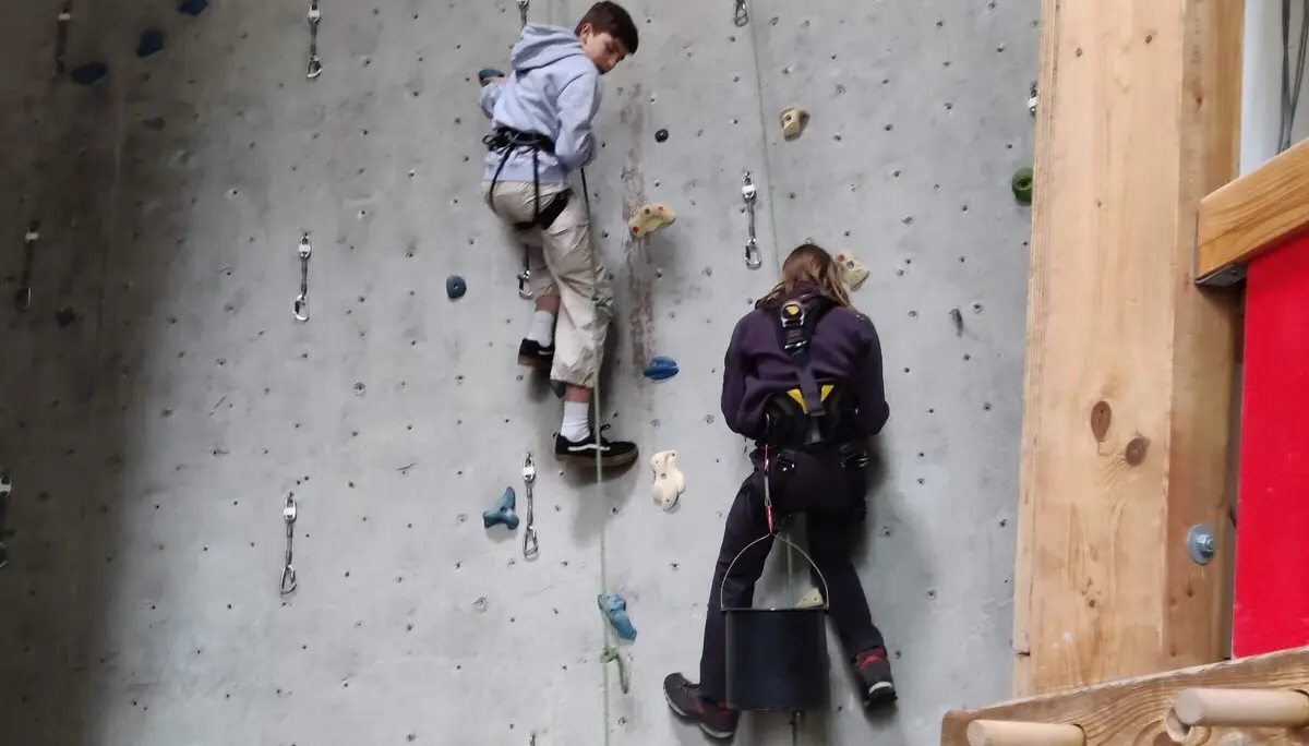 Zwei Personen arbeiten an einer Kletterwand mit bunten Griffen, tragen Sicherheitsgurte und Kletterausrüstung. | © DAV Markt Schwaben