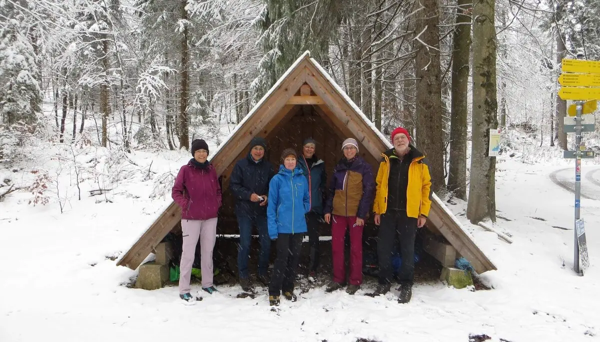 Gruppe vor Holzunterstand im verschneiten Wald – Winterwanderung mit Wegmarken und gemeinsamer Naturerfahrung. | © DAV Markt Schwaben | Foto Gerlinde Hübl