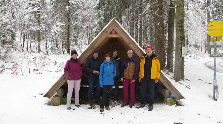 Gruppe vor Holzunterstand im verschneiten Wald – Winterwanderung mit Wegmarken und gemeinsamer Naturerfahrung. | © DAV Markt Schwaben | Foto Gerlinde Hübl