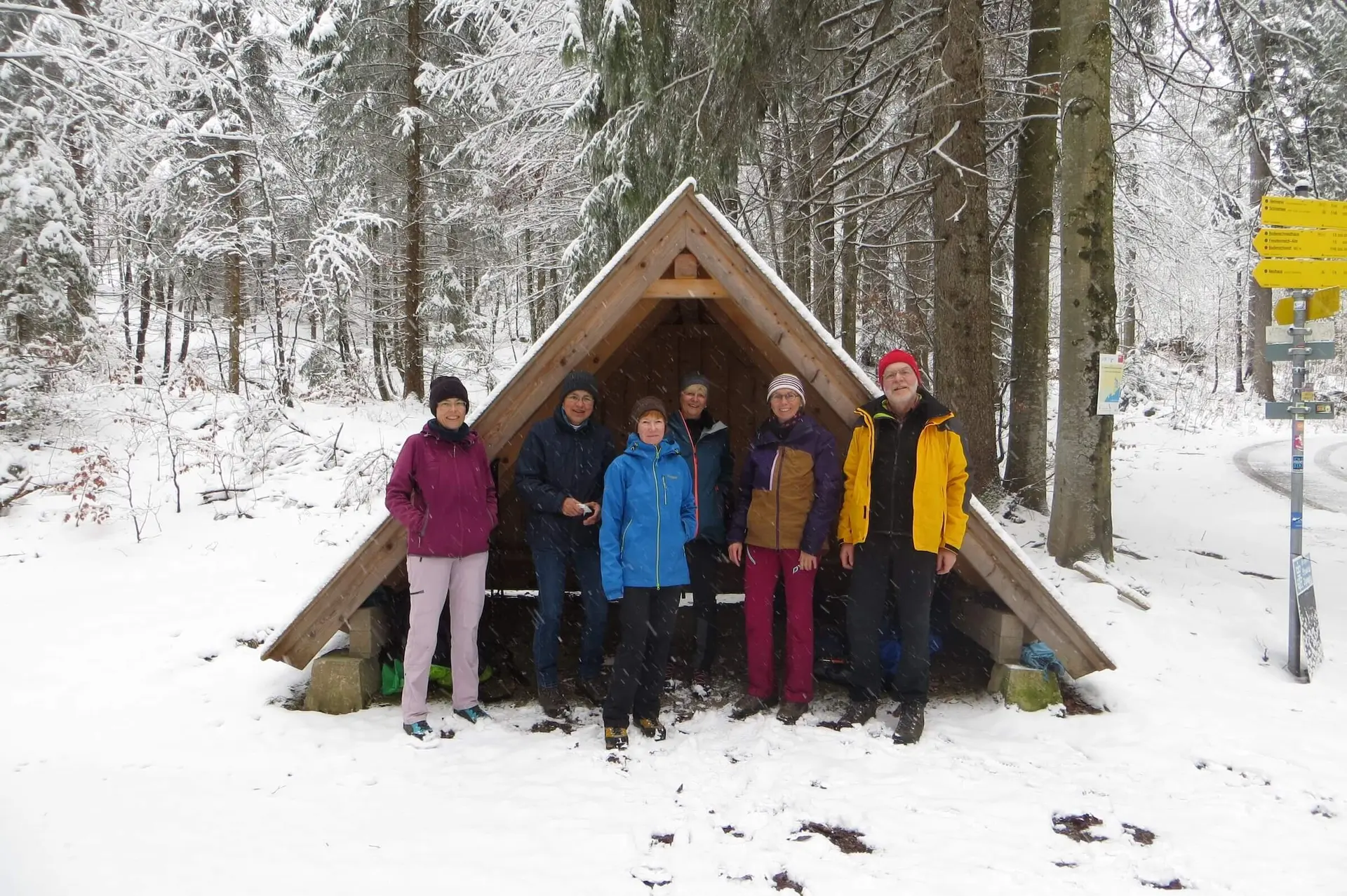 Gruppe vor Holzunterstand im verschneiten Wald – Winterwanderung mit Wegmarken und gemeinsamer Naturerfahrung. | © DAV Markt Schwaben | Foto Gerlinde Hübl