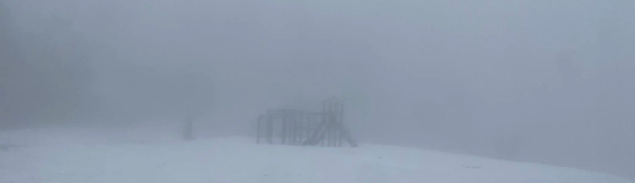 Spielplatzstruktur mit Rutsche und Kletterelementen, umgeben von Schnee und dichtem Nebel für eine mystische Atmosphäre. | © DAV Markt Schwaben