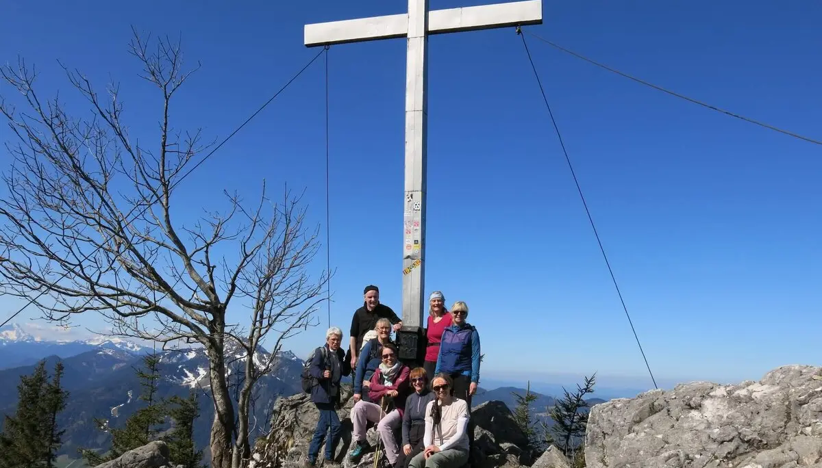 Gruppe von Wanderern auf felsigem Gipfel neben einem großen Metallkreuz. Klarer Himmel und Alpenpanorama im Hintergrund sorgen für eine beeindruckende Aussicht. | © DAV Markt Schwaben | Foto Erwin Matzinger