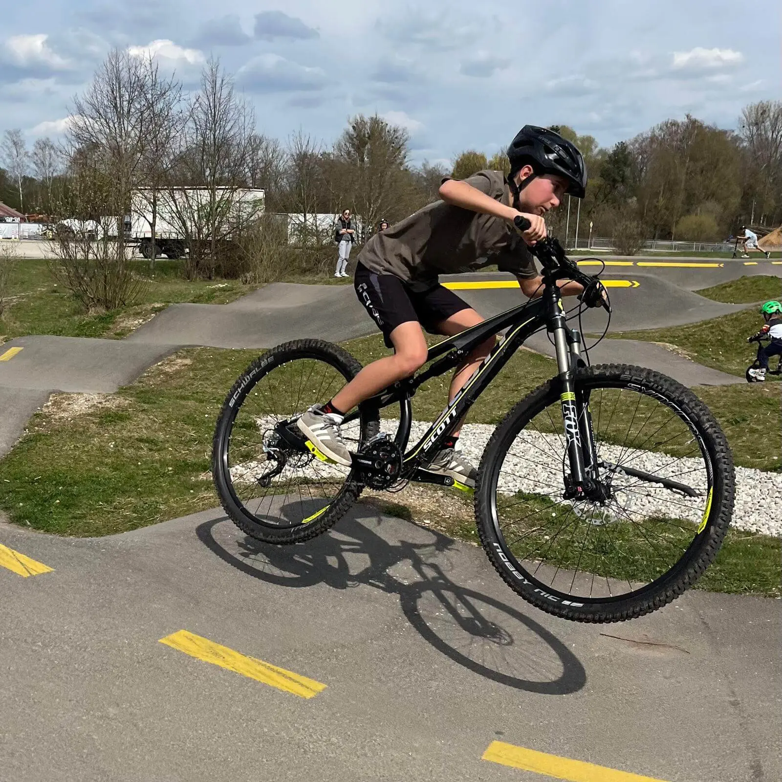 Kind macht Wheelie auf Pumptrack – Helm, Balance und Spaß auf kurviger Strecke mit gelben Pfeilen. | © DAV Markt Schwaben | Foto Miron Thoms
