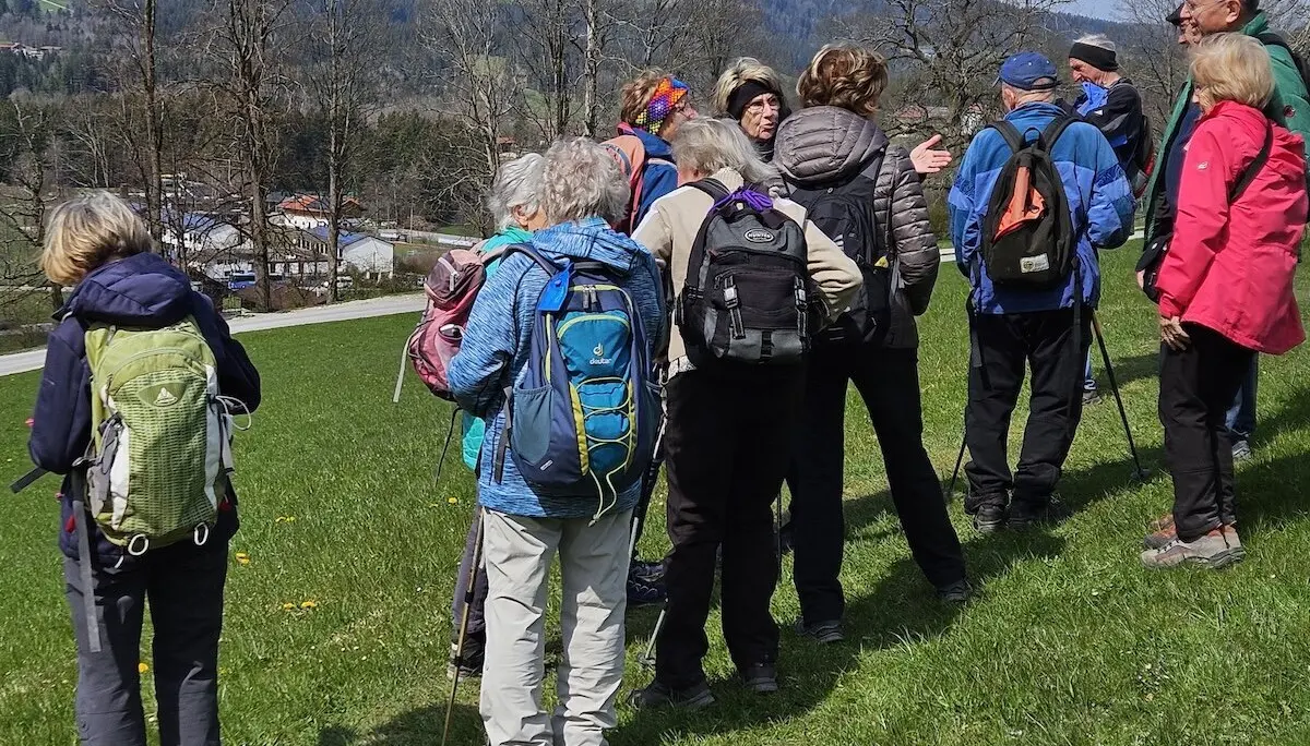 Wandergruppe mit Rucksäcken und Wanderstöcken steht auf einer Wiese mit Blick auf ein idyllisches Tal, umgeben von Bäumen und Hügeln. Ein schöner Moment der gemeinsamen Naturerkundung. | © DAV Markt Schwaben | Foto Hubert Inhofer