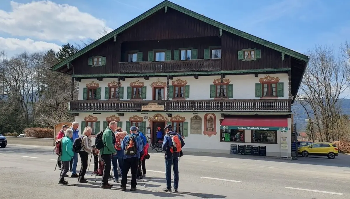 Wandergruppe steht vor einem traditionellen Gasthaus mit grünen Fensterläden und dekorierter Fassade, bereit für eine Tour in die umliegenden Berge. | © DAV Markt Schwaben | Foto Hubert Inhofer